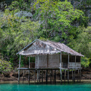 Vieille cabane sur pilotis au toit de chaume contre une falaise calcaire, Waigeo, Raja Ampat, Indonésie