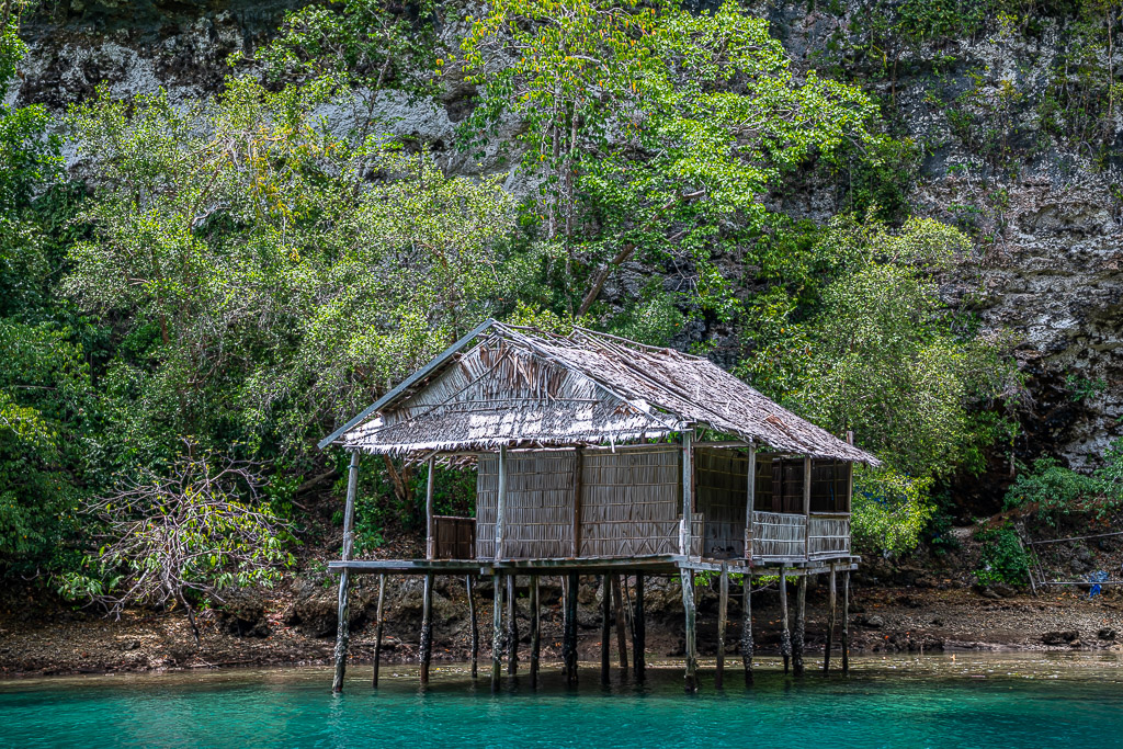 Vieille cabane sur pilotis au toit de chaume contre une falaise calcaire, Waigeo, Raja Ampat, Indonésie