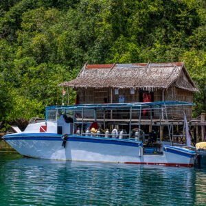 Dive boat moored at a jetty beside thatched stilt huts, Waigeo, Raja Ampat, Indonesia