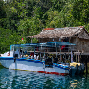 Dive boat with tanks moored at a stilt hut jetty, closer framing, Waigeo, Raja Ampat, Indonesia