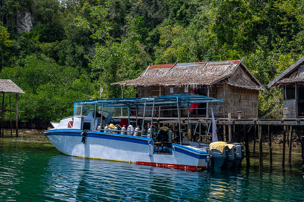 Dive boat with tanks moored at a stilt hut jetty, closer framing, Waigeo, Raja Ampat, Indonesia