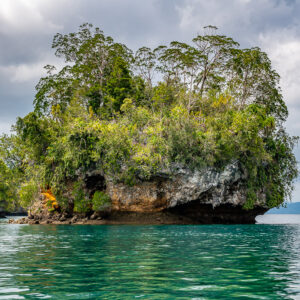 Mushroom islet with orange rock face before a distant pinnacle, Waigeo, Raja Ampat, Indonesia