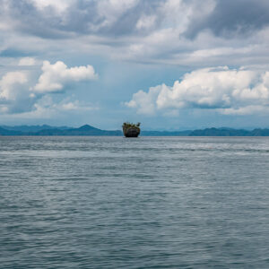 Tiny rock pinnacle on a wide bay with distant mountains, Waigeo, Raja Ampat, Indonesia