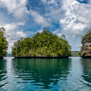 Islet framed by two limestone cliffs with reflections in turquoise water, Waigeo, Raja Ampat, Indonesia