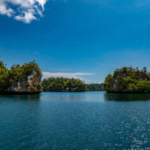 Two forested islets separated by a channel under a wide blue sky, Waigeo, Raja Ampat, Indonesia