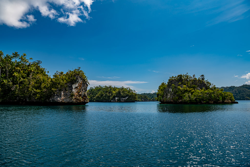 Two forested islets separated by a channel under a wide blue sky, Waigeo, Raja Ampat, Indonesia