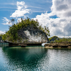 Undercut islet with flat rock ledges, reflections and cumulus clouds, Waigeo, Raja Ampat, Indonesia