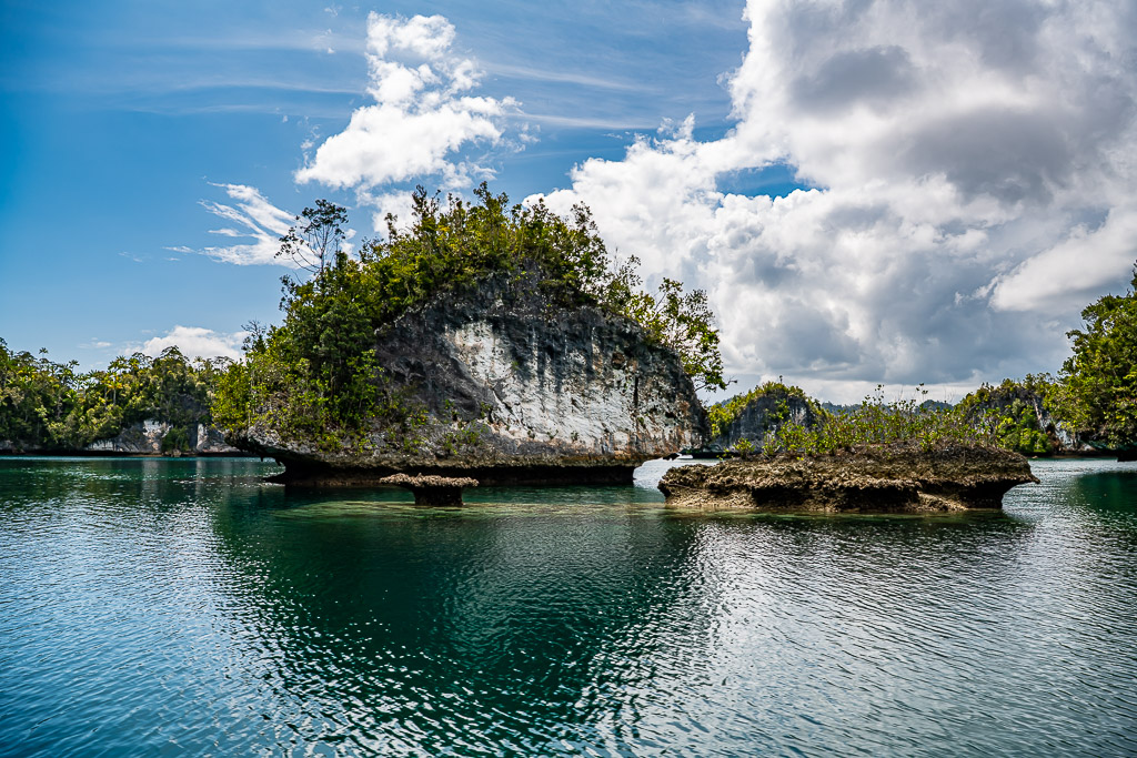 Undercut islet with flat rock ledges, reflections and cumulus clouds, Waigeo, Raja Ampat, Indonesia