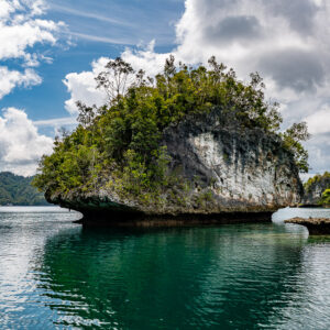Mushroom-shaped islet with white cliffs and a tiny rock under cumulus, Waigeo, Raja Ampat, Indonesia