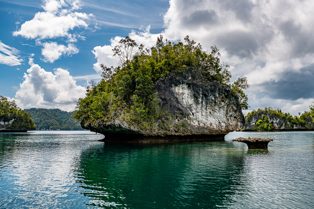 Mushroom-shaped islet with white cliffs and a tiny rock under cumulus, Waigeo, Raja Ampat, Indonesia