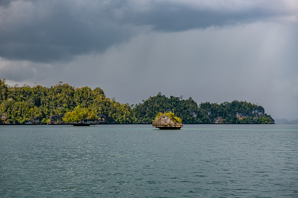 Rain curtain over a forested coast with a small rock at sea, Waigeo, Raja Ampat, Indonesia