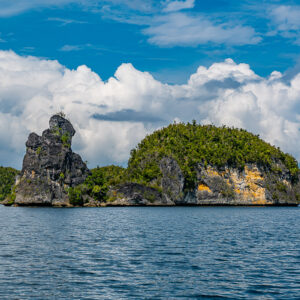Aiguille rocheuse à côté d’un îlot arrondi aux falaises ocre sous les cumulus, Waigeo, Raja Ampat, Indonésie