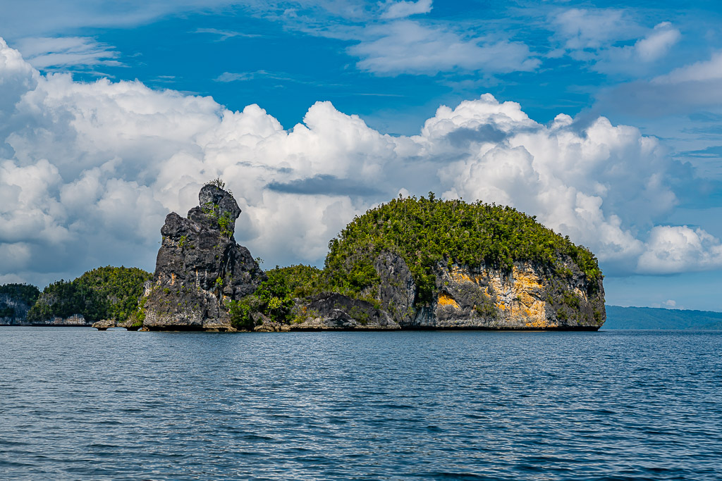 Aiguille rocheuse à côté d’un îlot arrondi aux falaises ocre sous les cumulus, Waigeo, Raja Ampat, Indonésie