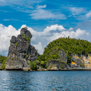 Vue plus rapprochée d’une haute aiguille rocheuse et d’un îlot arrondi sur une mer bleue, Waigeo, Raja Ampat, Indonésie