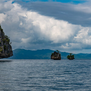 Cliff in foreground and two small rock islets with mountains behind, Waigeo, Raja Ampat, Indonesia