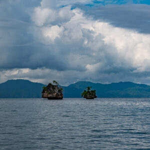 Two small rock islets before distant mountains under heavy clouds, Waigeo, Raja Ampat, Indonesia