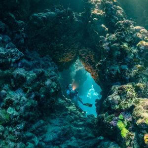 Rayons de soleil perçant une grotte récifale, plongeur au loin, vertical, Shaab Claudio, mer Rouge, Égypte