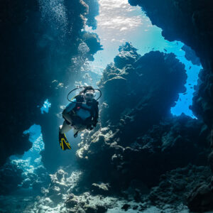 Woman diver in a cave passage below an opening to the surface, vertical, Shaab Claudio, Red Sea, Egypt