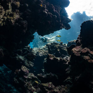 Woman diver passing beyond a dark cave arch, horizontal view, Shaab Claudio, Red Sea, Egypt