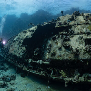 Diver with a torch beside the hull of a sunken sailboat, Red Sea, Egypt