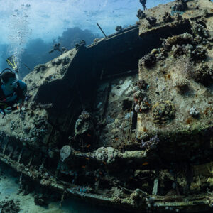 Woman diver with a torch alongside the sailboat wreck hull, close view, Red Sea, Egypt