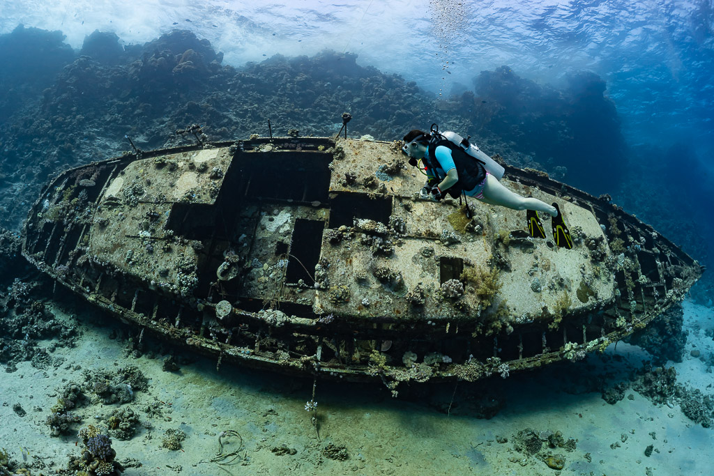 Woman diver gliding over the deck of a sunken sailboat wreck, Red Sea, Egypt