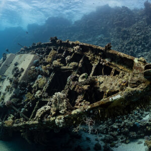 Sailboat wreck on the reef with distant divers and bubbles, Red Sea, Egypt