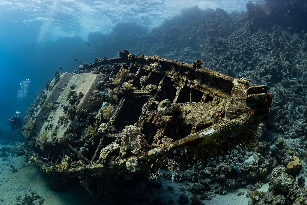Sailboat wreck on the reef with distant divers and bubbles, Red Sea, Egypt