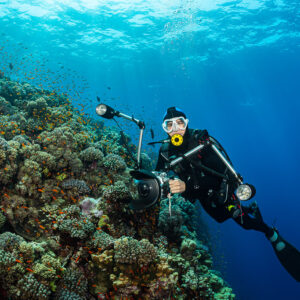 Diver with camera and strobes posing beside a coral slope, Habili Gafar, Red Sea, Egypt