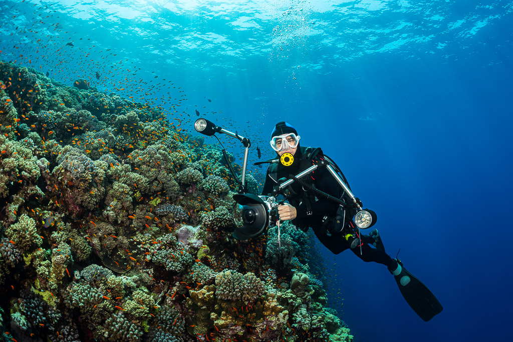 Diver with camera and strobes posing beside a coral slope, Habili Gafar, Red Sea, Egypt