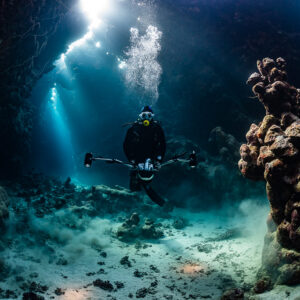 Underwater photographer with strobes in a cave lit by sunbeams and bubbles, Dangerous Reef South, Red Sea, Egypt