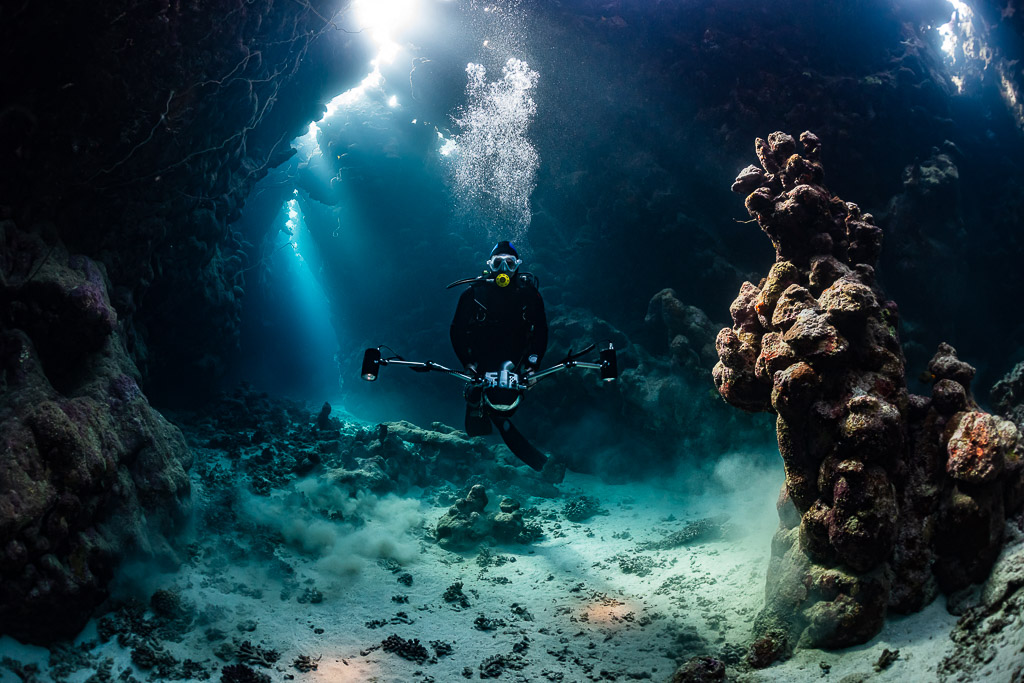 Underwater photographer with strobes in a cave lit by sunbeams and bubbles, Dangerous Reef South, Red Sea, Egypt