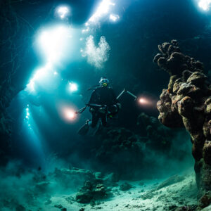 Underwater photographer with lights in a cave, strong sunbeams behind, Dangerous Reef South, Red Sea, Egypt