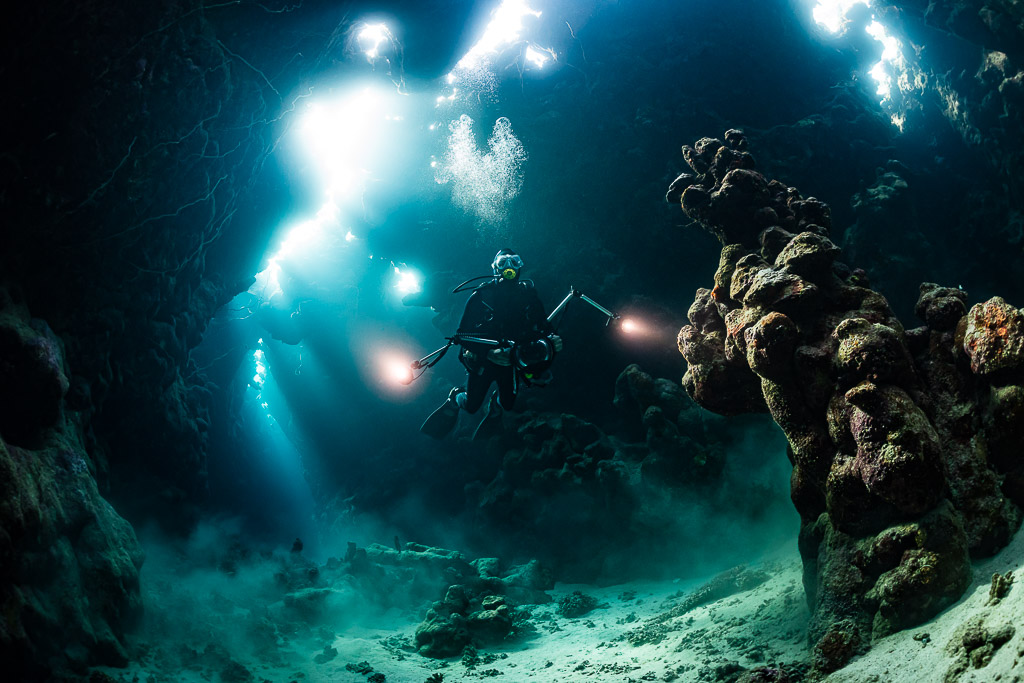 Underwater photographer with lights in a cave, strong sunbeams behind, Dangerous Reef South, Red Sea, Egypt