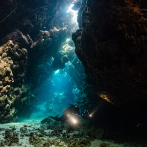 Diver with torch at the bottom of a dark cave beside a light shaft, Dangerous Reef South, Red Sea, Egypt