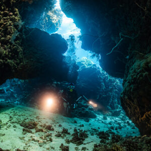 Divers with torches under a large rock arch inside a reef cave, Dangerous Reef South, Red Sea, Egypt