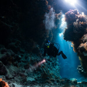 Diver with torch in a cave under sunbeams streaming through the roof, St John's Caves, Red Sea, Egypt