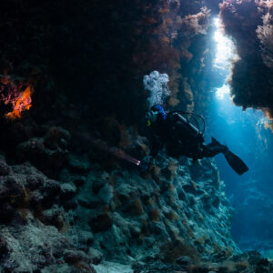 Diver exhaling bubbles in a cave passage lit by blue light, St John's Caves, Red Sea, Egypt