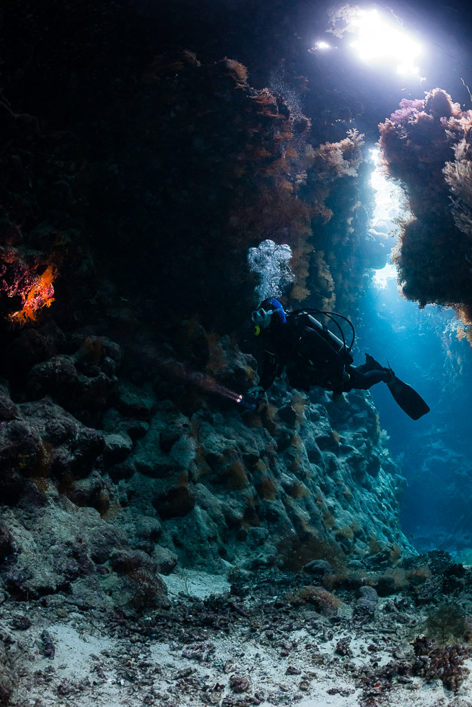 Diver exhaling bubbles in a cave passage lit by blue light, St John's Caves, Red Sea, Egypt