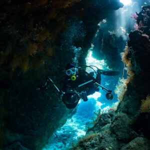 Underwater photographer framed in a slanted cave opening with blue light, St John's Caves, Red Sea, Egypt