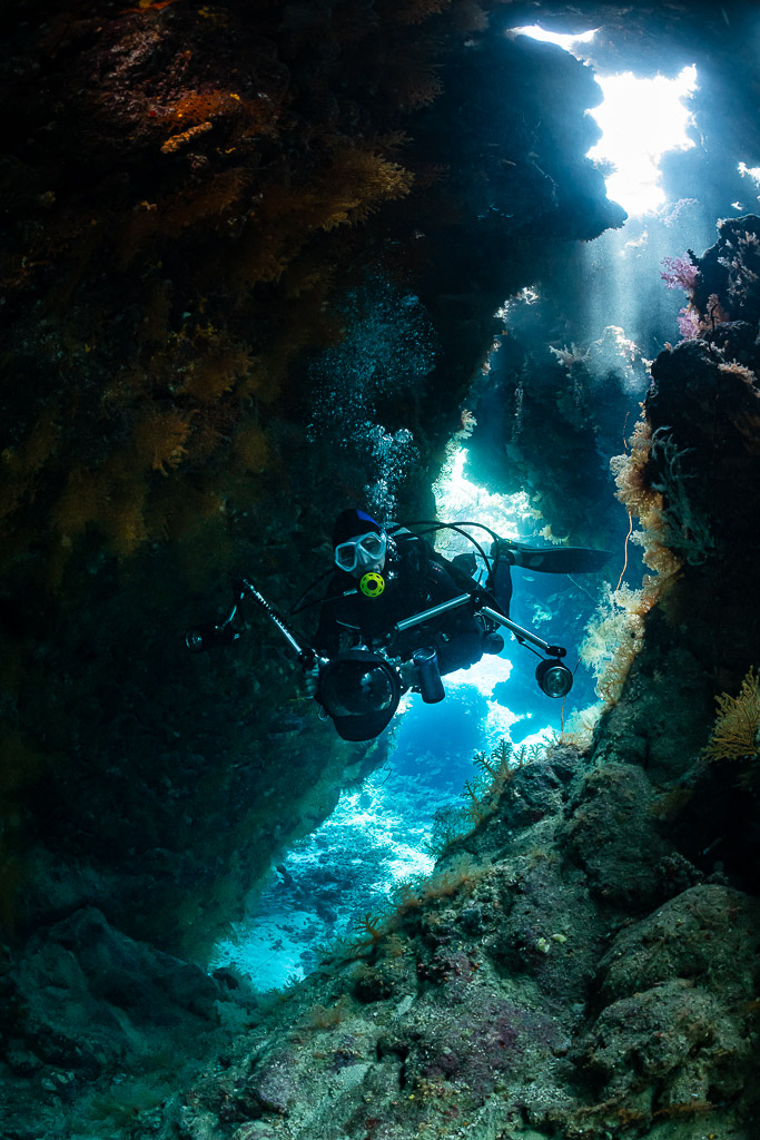 Underwater photographer framed in a slanted cave opening with blue light, St John's Caves, Red Sea, Egypt