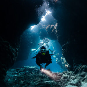 Diver with torch facing the camera in a narrow cave chimney, St John's Caves, Red Sea, Egypt