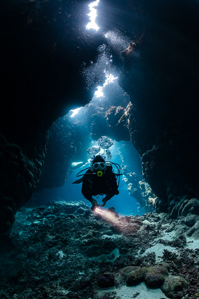 Diver with torch facing the camera in a narrow cave chimney, St John's Caves, Red Sea, Egypt