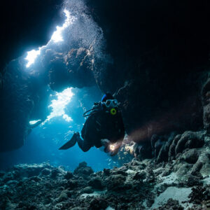 Diver silhouetted in a cave with bubbles rising toward light openings, St John's Caves, Red Sea, Egypt