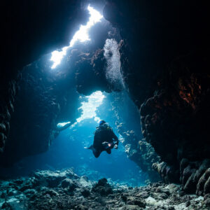 Small diver silhouette at the end of a cave tunnel with light shafts, St John's Caves, Red Sea, Egypt