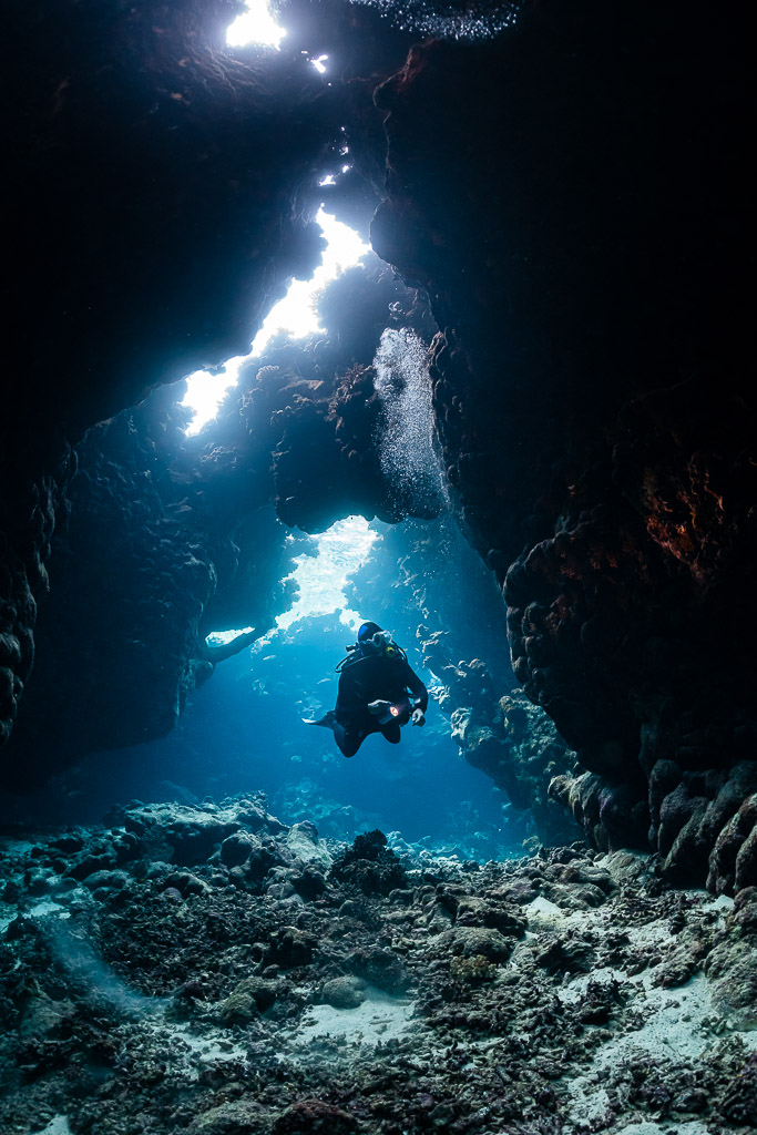 Small diver silhouette at the end of a cave tunnel with light shafts, St John's Caves, Red Sea, Egypt