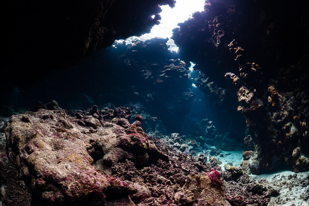 Wide view of a low reef cave with a bright opening and rocky floor, St John's Caves, Red Sea, Egypt