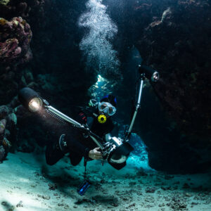 Underwater photographer with strobes exploring a cave, bubbles rising, St John's Caves, Red Sea, Egypt