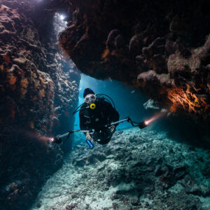 Diver with torches at a cave exit, closer framing, St John's Caves, Red Sea, Egypt