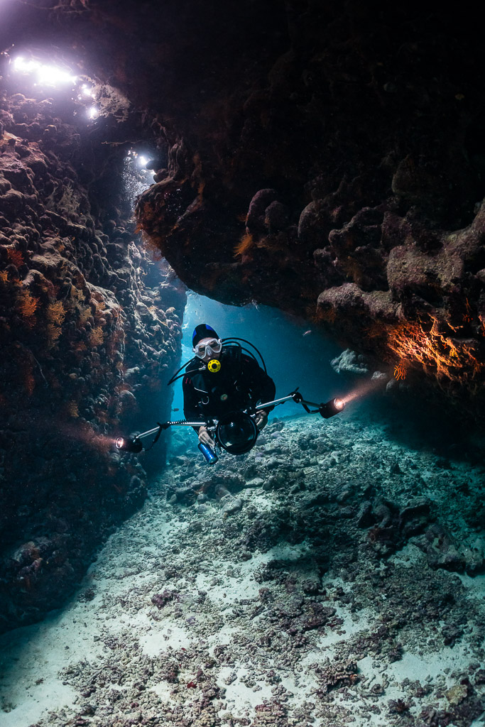 Diver with torches at a cave exit, closer framing, St John's Caves, Red Sea, Egypt